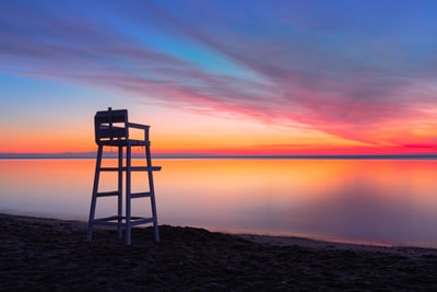 日落时，靠近水体的棕色沙滩上的棕色木椅